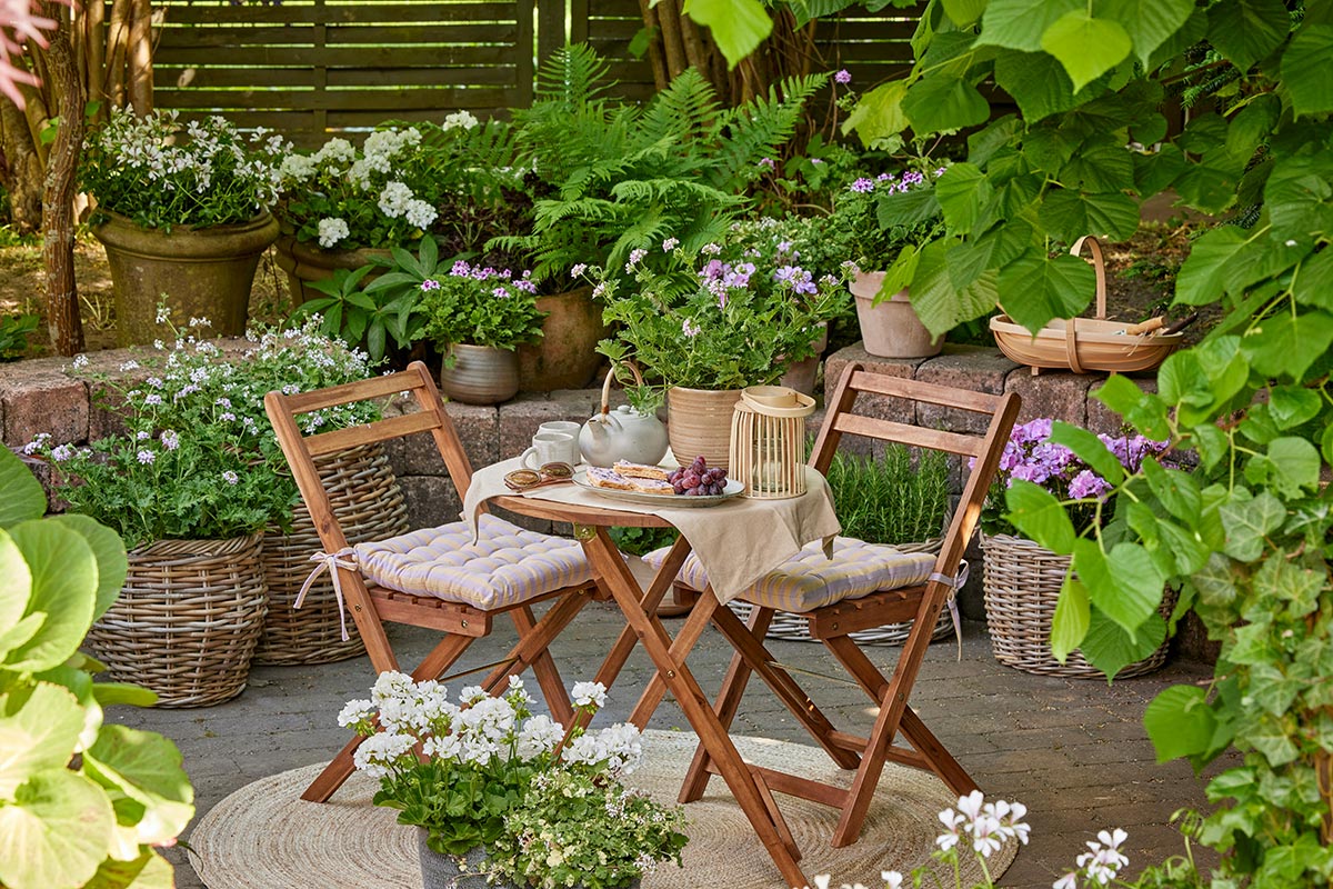 Acogedor rinc&oacute;n de jard&iacute;n con mesa redonda, sillas de madera y plantas en macetas alrededor